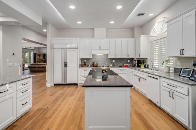 kitchen with white dishwasher, sink, paneled refrigerator, a kitchen island, and white cabinetry