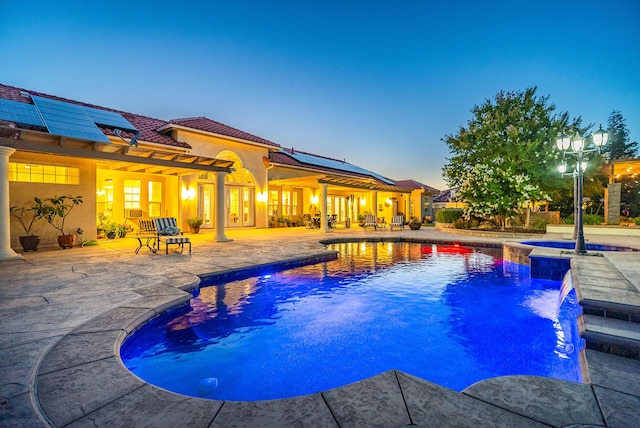 pool at dusk featuring pool water feature, an in ground hot tub, and a patio