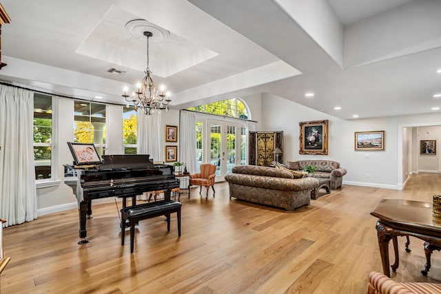 interior space featuring a chandelier, light wood-type flooring, french doors, and a tray ceiling