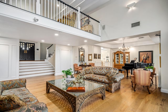 living room featuring a towering ceiling, a chandelier, and light wood-type flooring