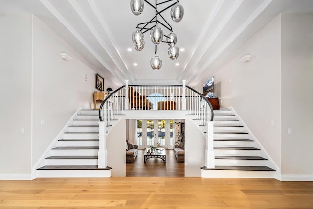 stairway with french doors, wood-type flooring, and a notable chandelier