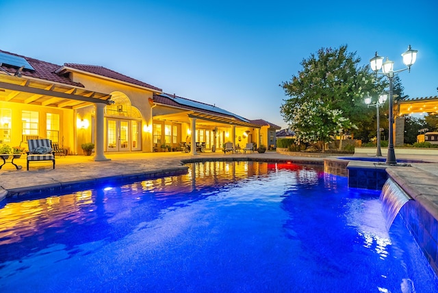 pool at dusk with french doors and a patio