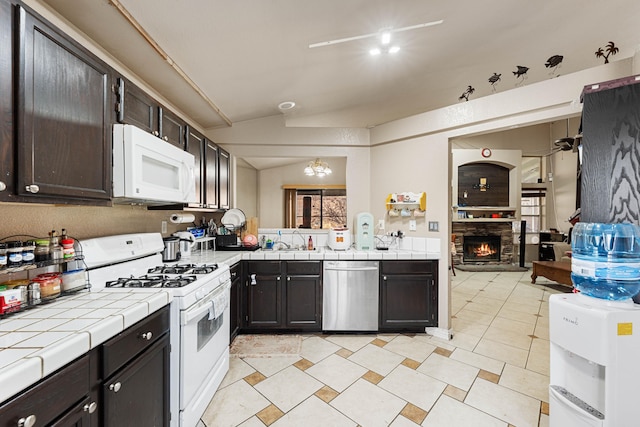 kitchen featuring vaulted ceiling, a fireplace, white appliances, dark brown cabinetry, and tile counters