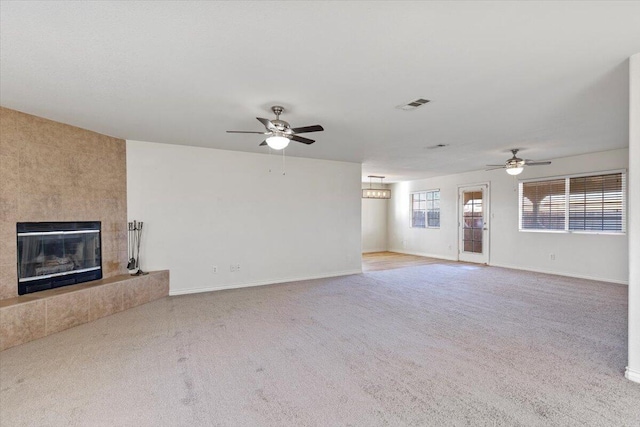 unfurnished living room with a ceiling fan, a tiled fireplace, visible vents, and carpet flooring