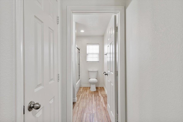 bathroom with toilet, shower / bath combination with glass door, baseboards, and wood finished floors