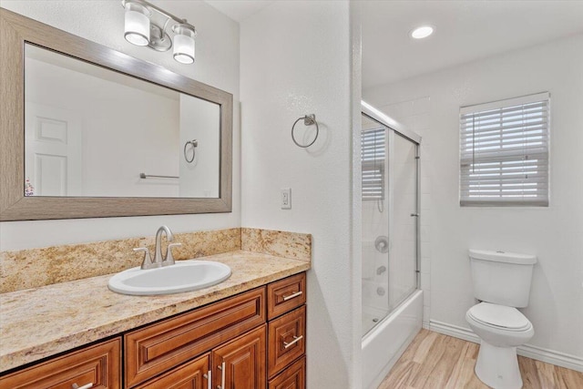 bathroom featuring baseboards, toilet, shower / bath combination with glass door, wood finished floors, and vanity