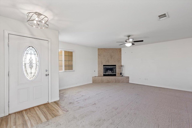 entrance foyer featuring baseboards, visible vents, carpet, a fireplace, and ceiling fan with notable chandelier