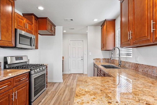 kitchen with a sink, visible vents, appliances with stainless steel finishes, light stone countertops, and light wood finished floors