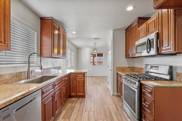 kitchen featuring light wood-style floors, appliances with stainless steel finishes, brown cabinetry, and a sink