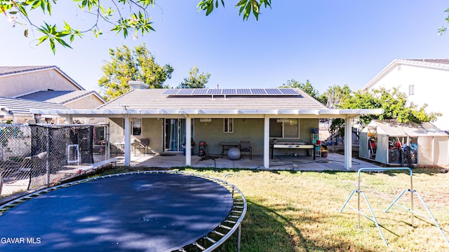 2839 Minford St, Lancaster, CA 93536 - back of house featuring a trampoline, a patio, a fenced backyard, roof mounted solar panels, and stucco siding