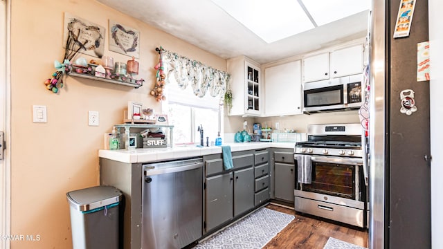 2839 Minford St, Lancaster, CA 93536 - kitchen featuring appliances with stainless steel finishes, gray cabinetry, dark wood-style flooring, tile countertops, and glass insert cabinets
