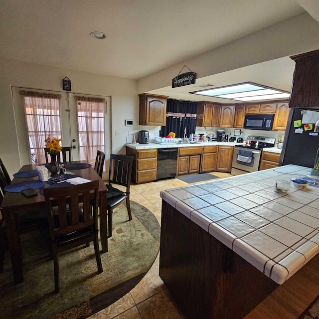 kitchen with light tile patterned floors, tile countertops, kitchen peninsula, black appliances, and sink