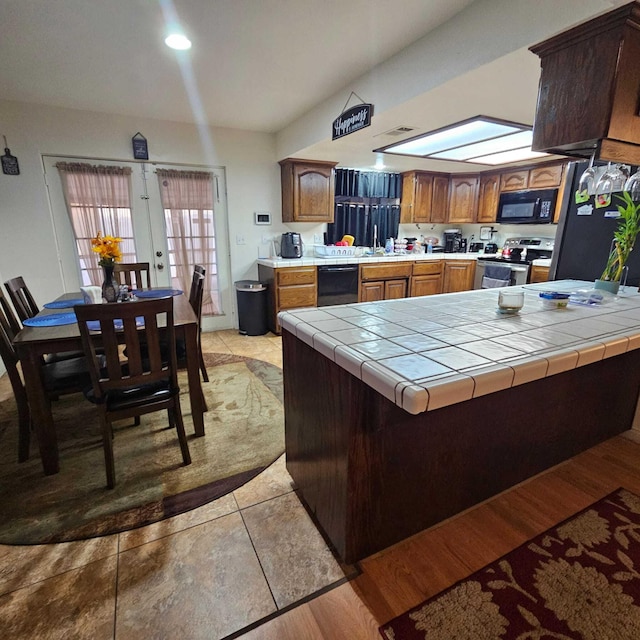 kitchen with a skylight, tile counters, french doors, black appliances, and sink