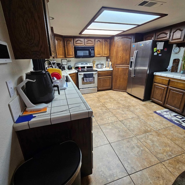 kitchen featuring a skylight, appliances with stainless steel finishes, and tile countertops