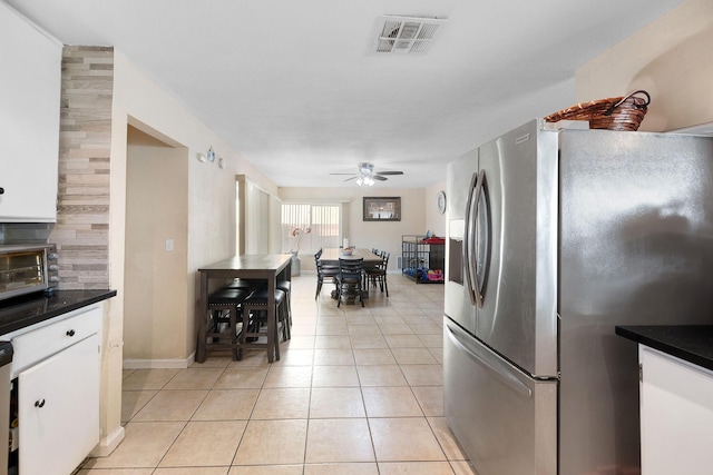 kitchen featuring stainless steel fridge, white cabinets, light tile patterned floors, and ceiling fan