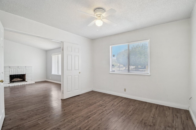 unfurnished living room with a brick fireplace, a textured ceiling, a ceiling fan, baseboards, and wood finished floors