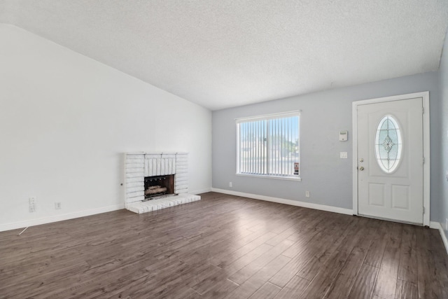 unfurnished living room featuring a brick fireplace, dark wood-style flooring, a textured ceiling, and baseboards