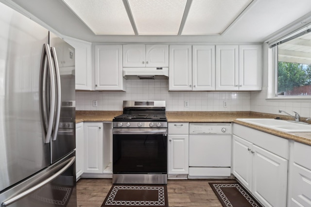 kitchen with wood finished floors, white cabinetry, under cabinet range hood, a sink, and stainless steel appliances