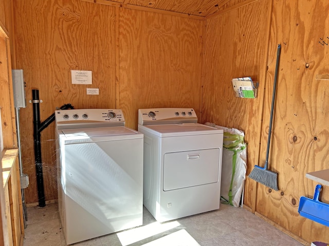 clothes washing area with washing machine and dryer and wood walls