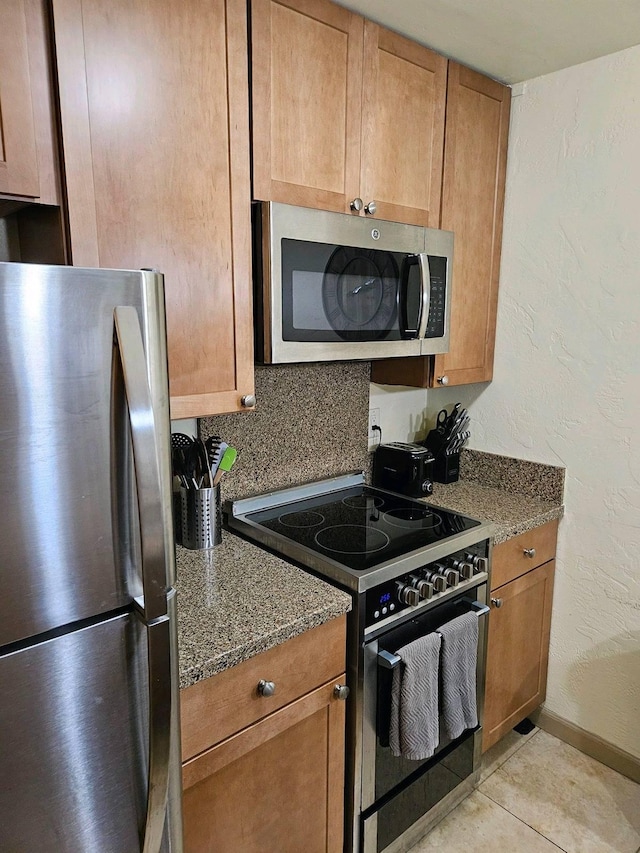 525 Aleka Lp Unit K3, Kapaa, HI 96746 - kitchen featuring appliances with stainless steel finishes, dark stone countertops, light tile patterned flooring, brown cabinetry, and a textured wall