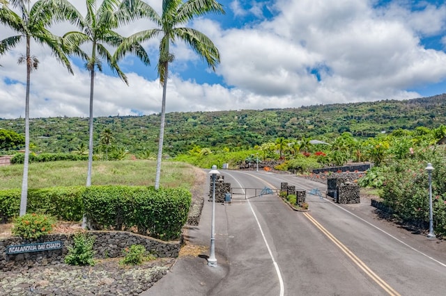83-1008 Kahula Pl, Captain Cook, HI 96704 - view of asphalt road with a view of trees, a gate, and street lighting