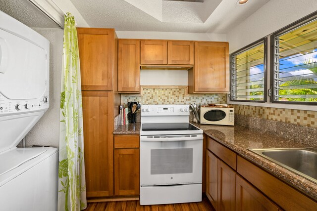 4480 Ka Haku Rd Unit 204, Princeville, HI 96722 - kitchen featuring white appliances, stacked washer and clothes dryer, decorative backsplash, brown cabinetry, and dark wood-style flooring