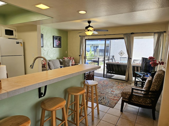 75-6082 Alii Dr Unit A201, Kailua-Kona, HI 96740 - kitchen with freestanding refrigerator, tile counters, light tile patterned floors, a breakfast bar area, and ceiling fan