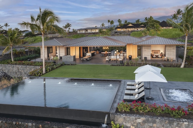 73-2210 Ala Kohanaiki, Kailua Kona, HI 96740 - back of house at dusk with metal roof, a lawn, a standing seam roof, an outdoor hangout area, and a patio