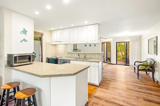 2721 Poipu Rd Unit 100, Koloa, HI 96756 - kitchen featuring stainless steel appliances, a peninsula, white cabinetry, light wood-style floors, and recessed lighting