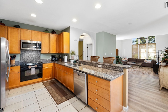 69-555 Waikoloa Beach Dr Unit 2605, Waikoloa, HI 96738 - kitchen featuring appliances with stainless steel finishes, a sink, dark stone counters, arched walkways, and a peninsula