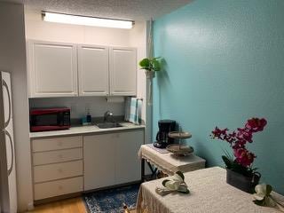 75-5680 Kuakini Hwy Unit 303, Kailua-Kona, HI 96740 - kitchen featuring black microwave, a sink, light countertops, white cabinets, and light wood-type flooring