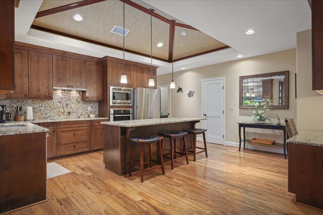 68-1122 Kaniku Dr Unit 111, Kamuela, HI 96743 - kitchen featuring stainless steel appliances, a raised ceiling, light wood-type flooring, a kitchen island, and a breakfast bar