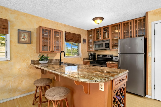 525 Aleka Lp Unit K12, Kapaa, HI 96746 - kitchen featuring appliances with stainless steel finishes, a sink, brown cabinets, light wood finished floors, and glass insert cabinets