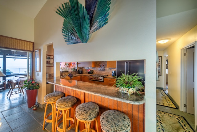 78-6928 Walua Rd, Kailua-Kona, HI 96740 - kitchen featuring brown cabinets, high end fridge, a peninsula, a towering ceiling, and tasteful backsplash