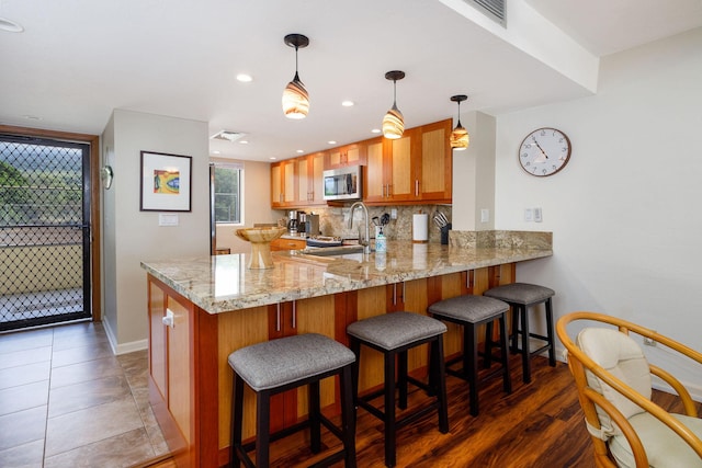 76-6225 Alii Dr Unit 105, Kailua-Kona, HI 96740 - kitchen featuring stainless steel microwave, a peninsula, baseboards, light stone counters, and brown cabinetry