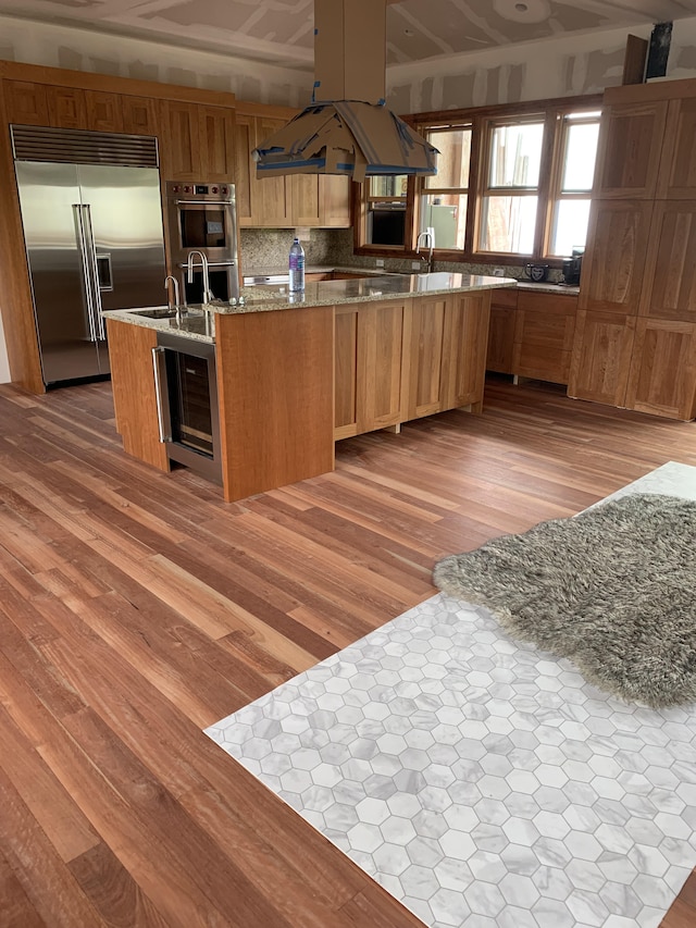 79-928 Mahiai Pl, Kealakekua, HI 96750 - kitchen featuring stainless steel appliances, light wood-type flooring, light stone countertops, tasteful backsplash, and a kitchen island with sink