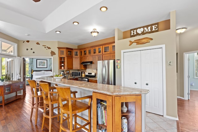 15-1932 2nd Ave, Keaau, HI 96749 - kitchen with stainless steel appliances, brown cabinetry, glass insert cabinets, a kitchen bar, and light stone counters