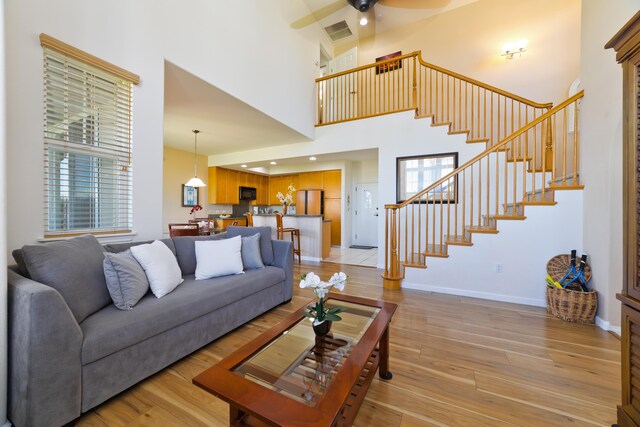 69-555 Waikoloa Beach Dr # 1701, Waikoloa, HI 96738 - living room featuring a towering ceiling, stairway, a ceiling fan, light wood finished floors, and baseboards