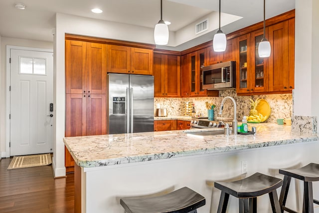 2611 Kiahuna Plantation Dr Unit 15F, Koloa, HI 96756 - kitchen with appliances with stainless steel finishes, a peninsula, glass insert cabinets, brown cabinetry, and decorative light fixtures