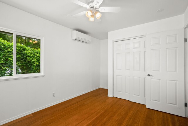 6450 Olohena Rd, Kapaa, HI 96746 - unfurnished bedroom featuring an AC wall unit, wood finished floors, a closet, baseboards, and ceiling fan