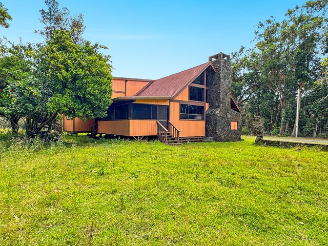 94-2664 Lorenzo Rd, Naalehu, HI 96772 - rear view of house with entry steps, a chimney, metal roof, and a yard