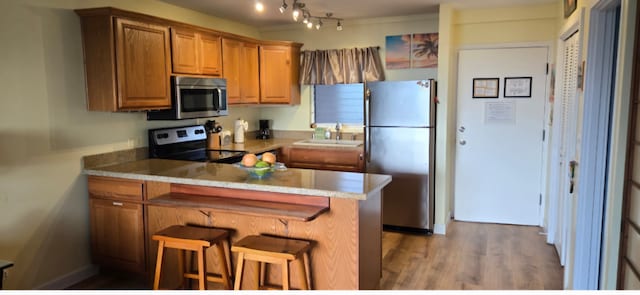 75-5766 Kuakini Hwy Unit 503, Kailua-Kona, HI 96740 - kitchen featuring stainless steel appliances, a sink, a peninsula, brown cabinetry, and wood finished floors