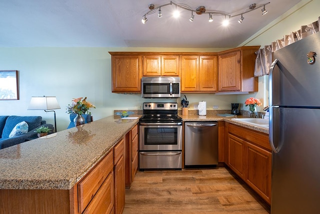 75-5766 Kuakini Hwy Unit 503, Kailua-Kona, HI 96740 - kitchen with appliances with stainless steel finishes, a peninsula, a sink, brown cabinetry, and light wood-style flooring