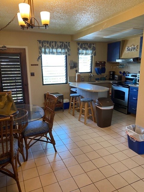 5061 Lawai Rd Unit 203, Koloa, HI 96756 - kitchen with electric stove, a textured ceiling, a peninsula, a chandelier, and light tile patterned flooring