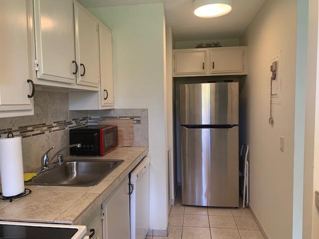 75-6026 Alii Dr Unit 5207, Kailua-Kona, HI 96740 - kitchen with freestanding refrigerator, white dishwasher, light tile patterned floors, baseboards, and tasteful backsplash
