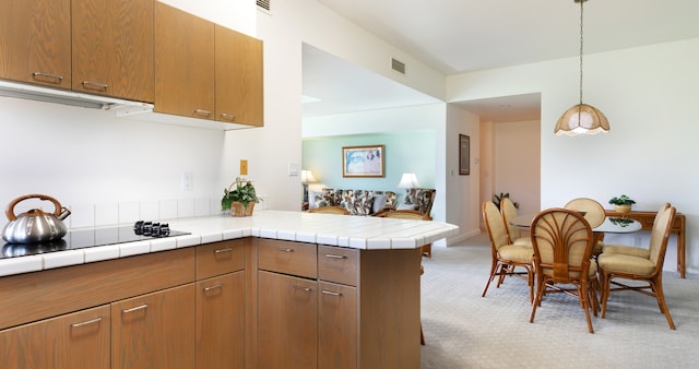 69-1010 Keana Pl Unit F105, Waikoloa, HI 96738 - kitchen featuring light colored carpet, black electric stovetop, brown cabinetry, a peninsula, and decorative light fixtures