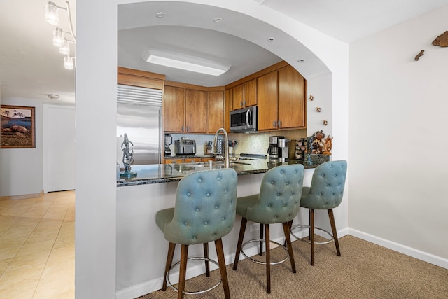 75-6106 Alii Dr Unit 208, Kailua-Kona, HI 96740 - kitchen featuring appliances with stainless steel finishes, brown cabinets, a sink, dark stone counters, and baseboards