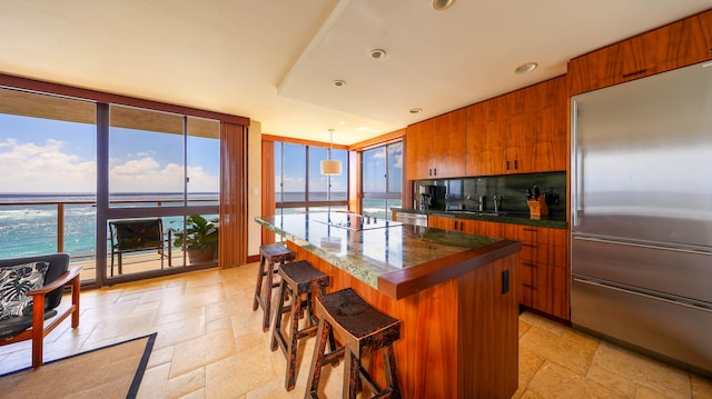 5050 Lawai Rd Unit 413, Koloa, HI 96756 - kitchen featuring appliances with stainless steel finishes, stone tile flooring, brown cabinets, a center island, and a wall of windows