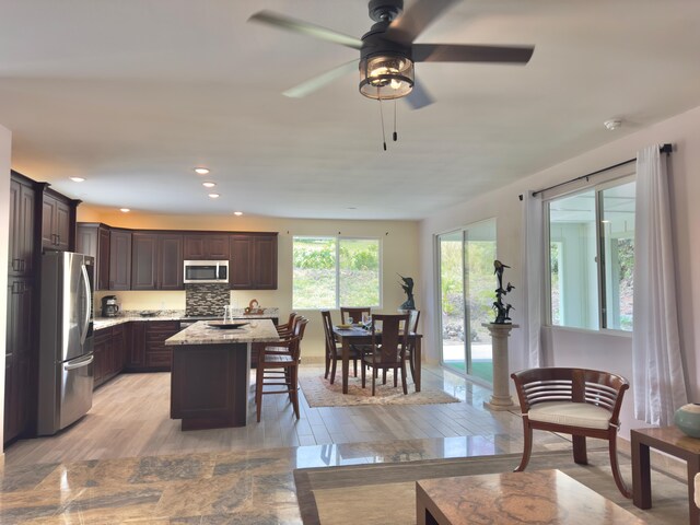 94-5763 Awa Pae Pl, Naalehu, HI 96772 - kitchen featuring appliances with stainless steel finishes, dark brown cabinets, a kitchen island, light wood finished floors, and a kitchen breakfast bar