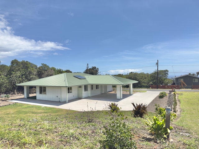 94-5763 Awa Pae Pl, Naalehu, HI 96772 - rear view of house featuring concrete driveway, a patio, roof mounted solar panels, metal roof, and board and batten siding